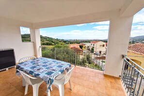 Varanda com mesa, cadeiras, televisão e vista para uma cidade e colinas.