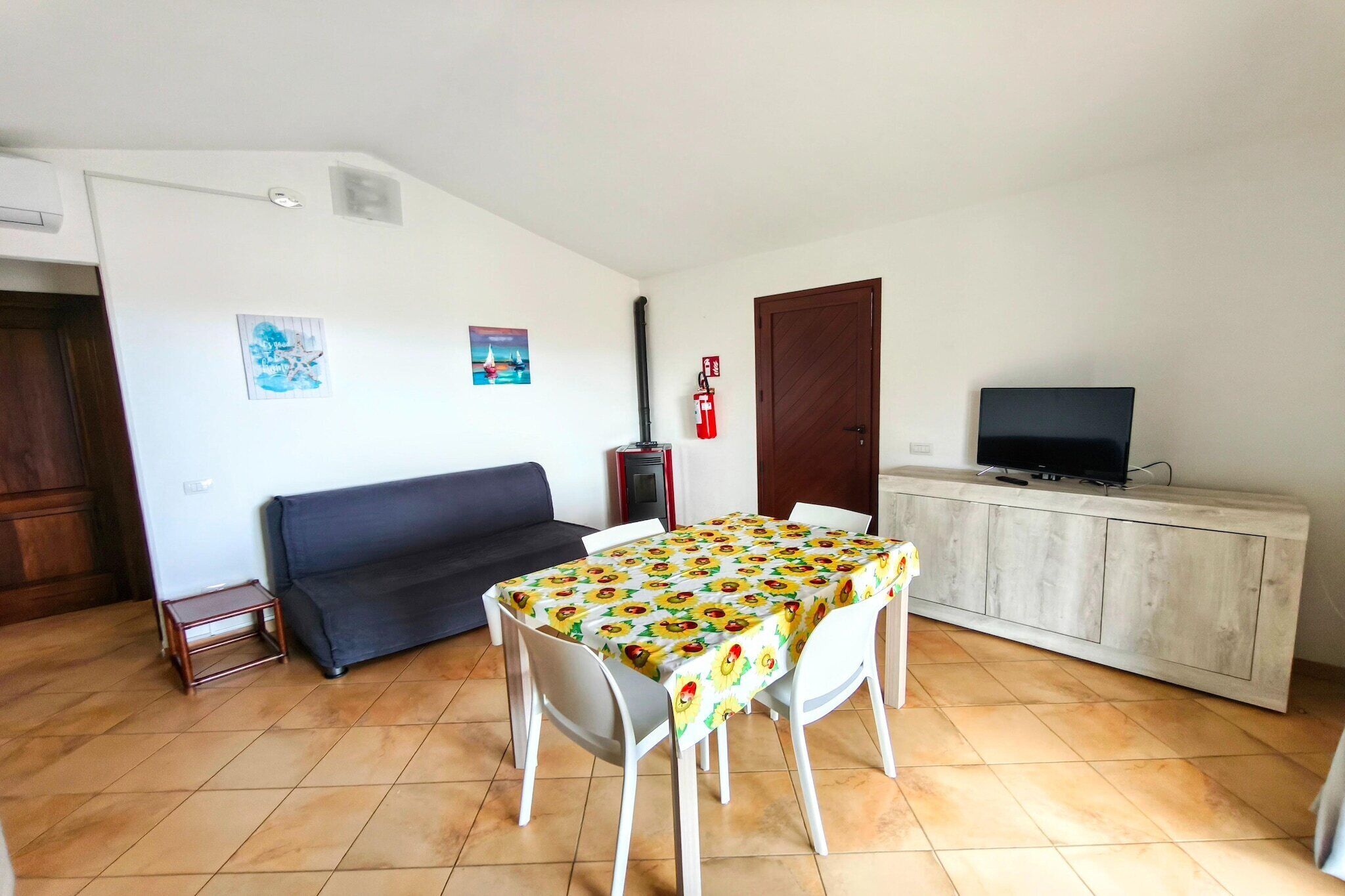 A living room with a sofa, a dining table with chairs, a television on a cabinet, and a small side table.