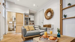 A modern living room with a sofa, a coffee table with croissants and juice, and a kitchen in the background. - Elegant Studio in 16th - Eiffel Tower & Trocadero (Paris)