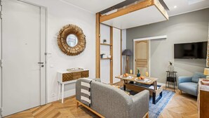 A modern living room with a sofa, a coffee table, a TV, and a dining area. - Elegant Studio in 16th - Eiffel Tower & Trocadero (Paris)