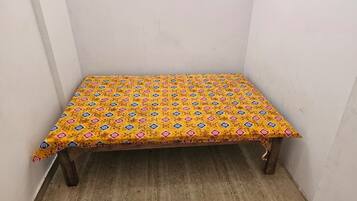 A small wooden table with a yellow patterned tablecloth in a corner of a room with plain white walls and a wooden floor.