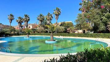A pool surrounded by palm trees and greenery, with buildings in the background.