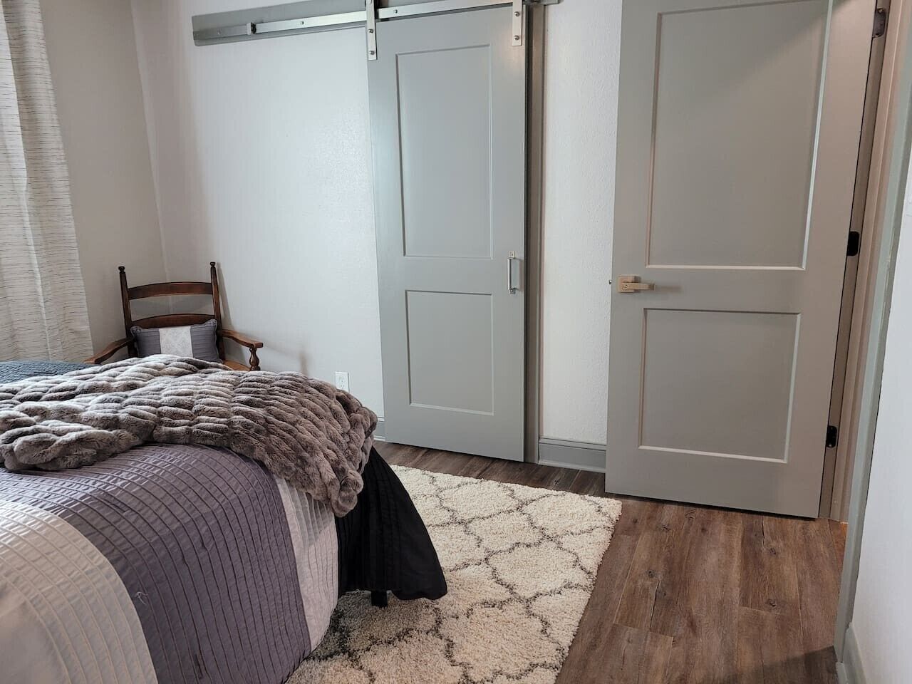 A bedroom with a bed, a chair, a wardrobe, and a door.
