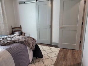 Een slaapkamer met een bed, een stoel, een kledingkast en een deur.