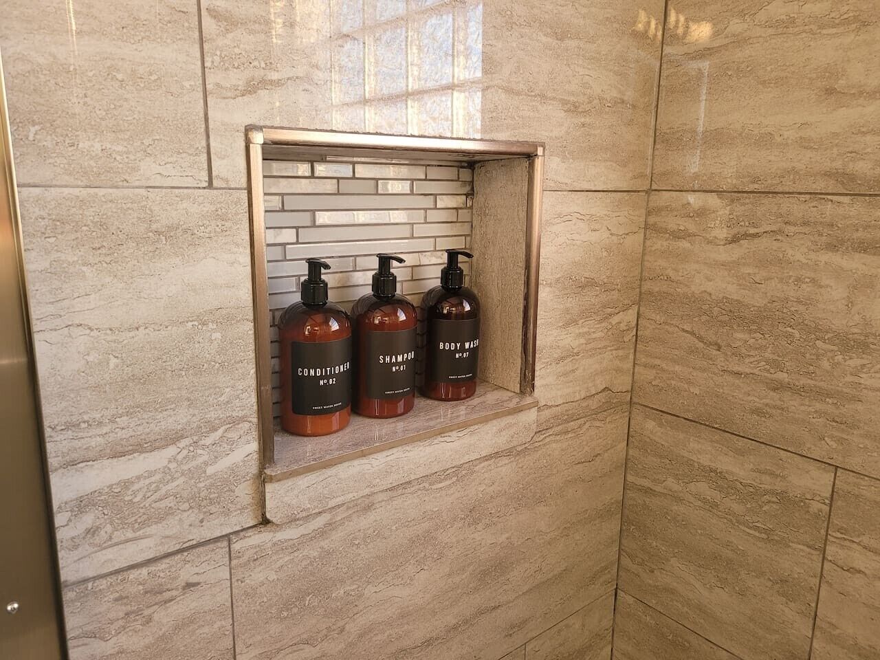 Un baño con pared de mármol y estante con tres artículos de aseo.