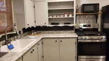 A kitchen with white cabinets, a stainless steel stove, and a microwave on a shelf.