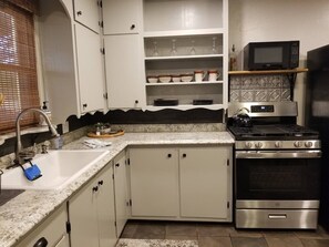 Una cocina con armarios blancos, una estufa de acero inoxidable y un microondas en un estante.