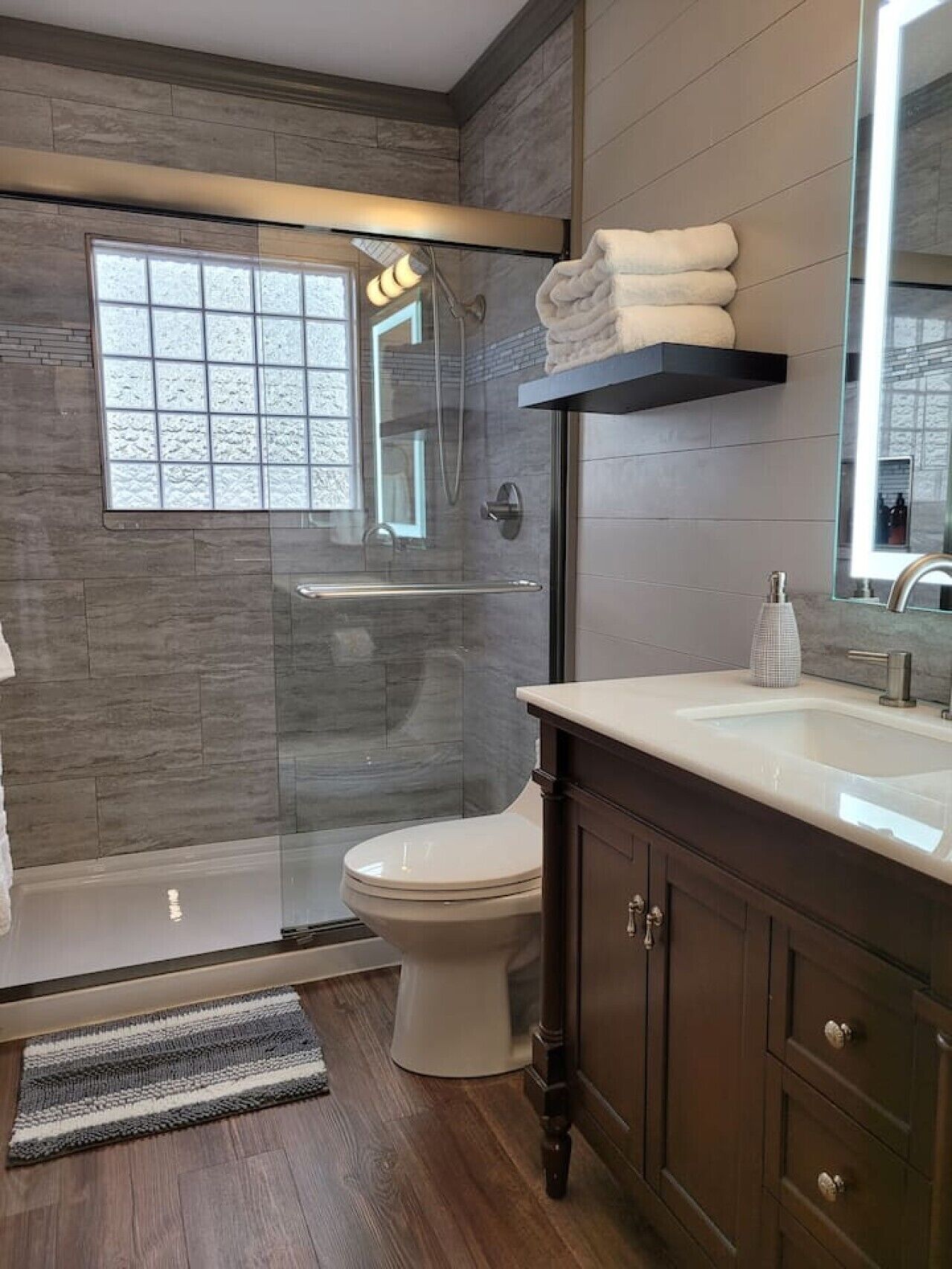 A modern bathroom with a glass shower enclosure, a toilet, a vanity with a mirror, and a window.