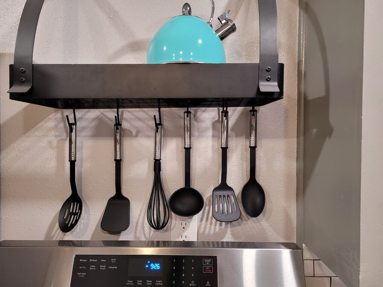 A kitchen with a stainless steel range hood, a blue kettle, and a wall-mounted utensil rack holding various kitchen tools.