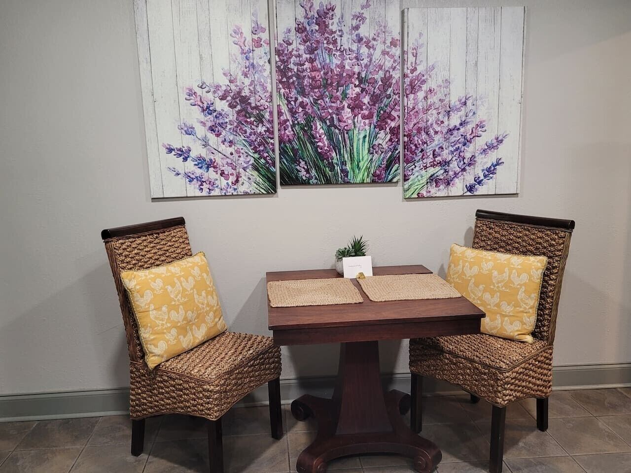 Un coin repas avec deux chaises en osier, une table en bois et une œuvre d’art aux motifs floraux accrochée au mur.