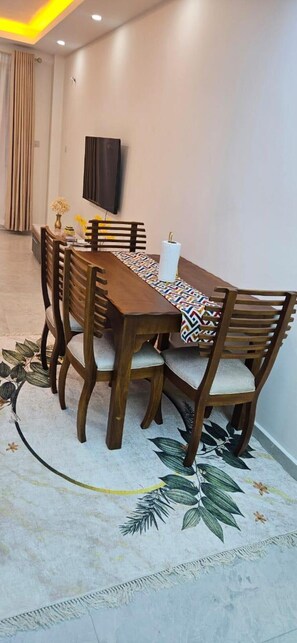 A dining area with a long wooden table, matching chairs, and a patterned table runner. - Modern 2BR with Pool Near Beach & City Mall, Nyali (Mombasa)