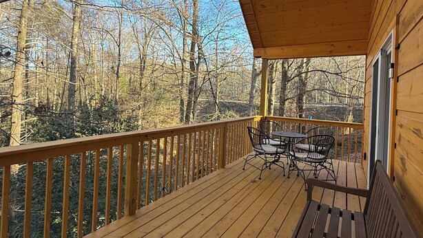 Une terrasse en bois avec un banc et des chaises, donnant sur une zone boisée.