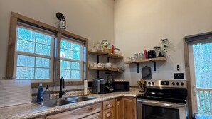 Une cuisine avec des meubles en bois, une cuisinière en acier inoxydable et une fenêtre donnant sur les arbres.
