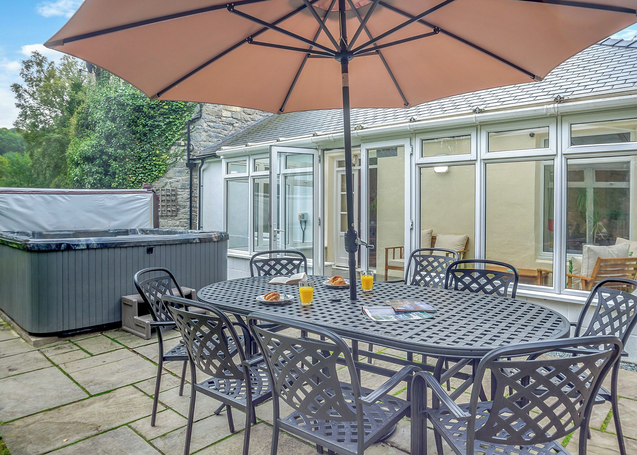 Une terrasse avec une table et des chaises, un jacuzzi et un grand parasol.