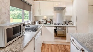 Een moderne keuken met witte kasten, een inbouwoven, een gasfornuis en een raam met uitzicht op een tuin.