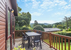 A wooden deck with a table and chairs, overlooking a lush landscape with trees and hills. - Modern and stylish timber clad holiday home with one double and two twin. (Bala,)