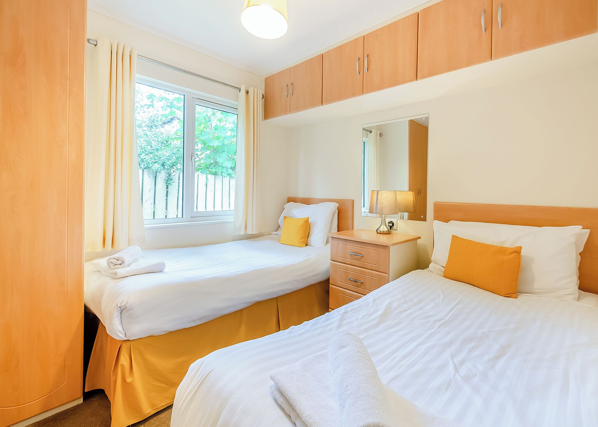 A hotel room with two beds, a nightstand, a mirror, and a window with curtains.