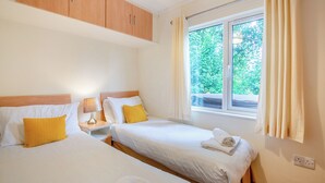 Een hotelkamer met twee bedden, een raam met gordijnen, een houten hoofdeinde en een nachtkastje met een lamp.