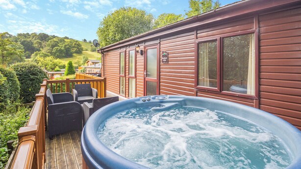 Een hottub op een houten terras met uitzicht op een huis en groen.