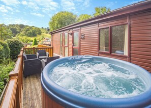 A hot tub on a wooden deck with a view of a house and greenery. - Modern and stylish timber clad holiday home with one double and two twin. (Bala,)