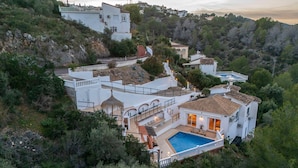 Una villa en una colina con piscina, jardín en terrazas y varios balcones.
