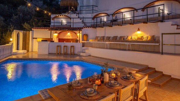 Un área de piscina exterior lujosa con zona de comedor, espacio de estar y una escalera que lleva a un nivel superior.