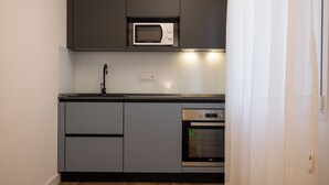 A compact kitchen with grey cabinets, a built-in microwave, a stainless steel oven, and a modern faucet. - Luxury Freedom Apollo (Palermo)