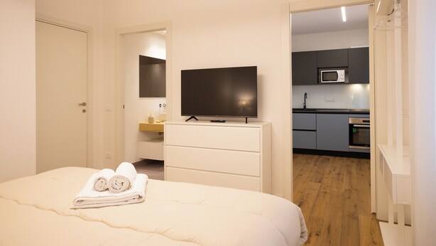 A bedroom with a bed, a TV on a dresser, and a view into the kitchen. - Luxury Freedom Apollo (Palermo)