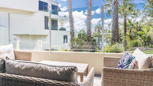 A balcony with wicker furniture, a view of a modern building, and tall palm trees. - Gorgeous 2-Bed Unit near Riverside Parks (Chiswick)