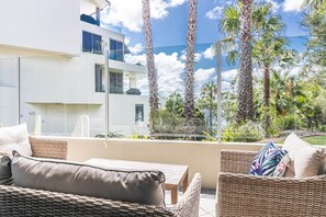 A balcony with wicker furniture, a view of a modern building, and tall palm trees. - Gorgeous 2-Bed Unit near Riverside Parks (Chiswick)