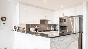 A modern kitchen with white cabinets, a marble island, stainless steel appliances, and a clock on the wall. - Gorgeous 2-Bed Unit near Riverside Parks (Chiswick)