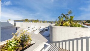 Una terraza en la azotea con sillones blancos, una jardinera de concreto con plantas y vistas al mar y a las colinas.