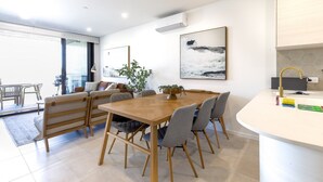Un comedor moderno con una mesa y sillas de madera, una planta en maceta y un cuadro de una casa en un acantilado.
