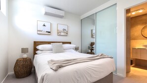 Un dormitorio con una cama grande, una lámpara de noche, aire acondicionado instalado en la pared y dos cuadros enmarcados.
