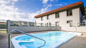 En udendørs swimmingpool med en metalstige, omgivet af en betonmur og et hegn.