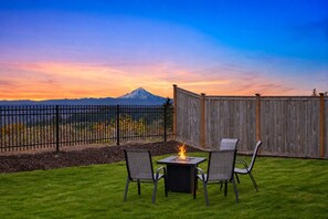 Un patio con dos sillas, una mesa, un hogar para fuego y vistas de una cadena montañosa.