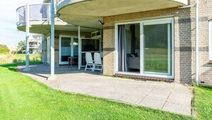 Un immeuble résidentiel doté d’un patio couvert, d’une porte-fenêtre coulissante et d’un petit espace extérieur aménagé avec des chaises.