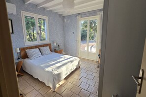 A bedroom with a bed, a nightstand, a lamp, and a window.