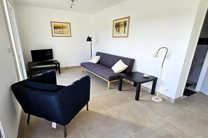 A modern living room with a sofa, two armchairs, a TV, and a floor lamp. - Inviting holiday home in Pierrerue (Pierrerue)