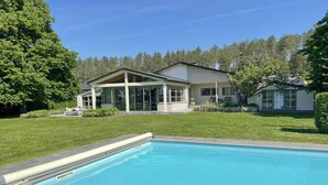 Une maison moderne dotée d’une piscine, entourée d’une pelouse bien entretenue et d’arbres.
