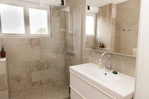 Een moderne badkamer met een douchecabine van glas, een witte wastafel en een grote spiegel.