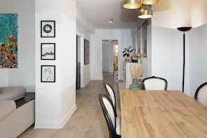 Een eethoek met een houten tafel, stoelen en kunstwerken in lijsten aan de muur.