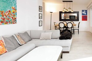 Een moderne woonkamer met een bank, een eettafel met stoelen, een vloerlamp en kunst aan de wanden.