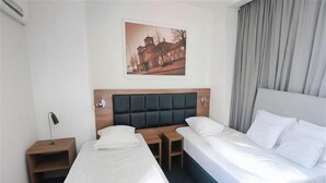Une chambre d’hôtel avec deux lits, une tête de lit, une table de chevet, une lampe, une petite table et un tableau encadré au mur.