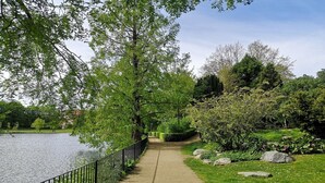 A pathway beside a body of water, surrounded by greenery and a fence.