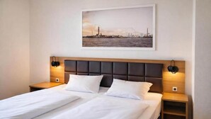 Een tweepersoonsbed met een houten hoofdbord, twee nachtkastjes en een lijst met een stadsgezicht erboven.