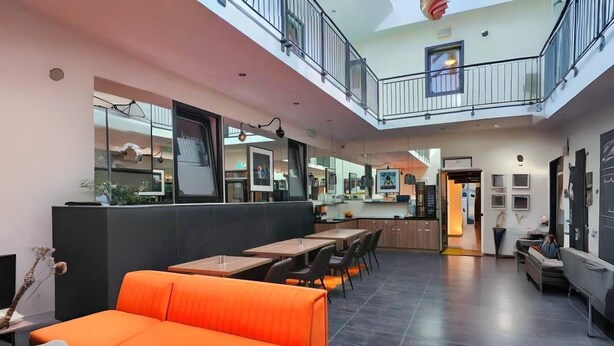 Een modern interieur met een hoge plafond, een entresol en een eethoek met oranje zitplaatsen.