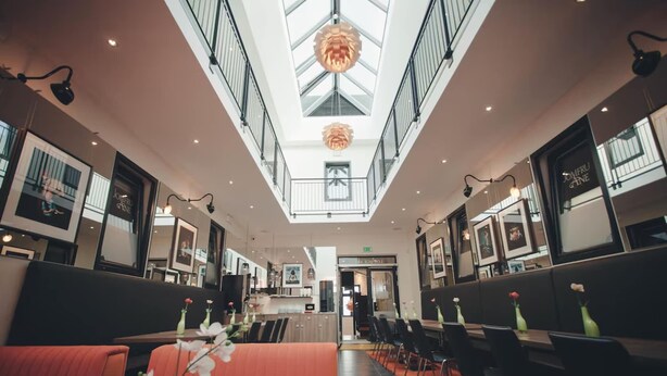 Un hall d’hôtel moderne, doté d’un plafond haut, d’un lustre central et d’un espace détente avec des tables et des chaises.