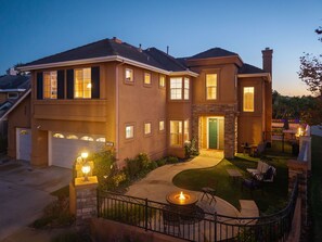 A two-story house with a stone facade, a green front door, and a landscaped front yard with a fire pit and outdoor seating. - Carmel Valley Villa by Coastline Vacation Rentals (San Diego)