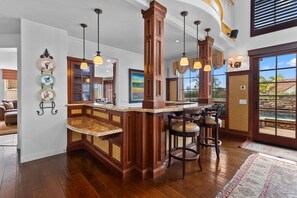 A kitchen with a wooden island, bar stools, pendant lighting, and a view of the outdoors. - Carmel Valley Villa by Coastline Vacation Rentals (San Diego)